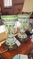Two Bohemian glass lustre lamps side by side on brass pedestal bases, showing overall pair
