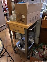 Butcher block cart with wheeled metal frame and a cardboard box on top, visible drawer and contents on lower shelves.