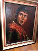 Framed painting of a young man wearing a colorful patterned sweater, dark background, signed P. James in bottom right corner.