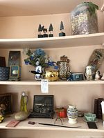 Shelf display showing silver-toned ink wells, ceramic vases with artificial flowers, trinket boxes, stained glass piece, and small decorative items including a ceramic figure and books.