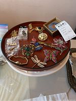 Top-down view of assorted costume jewelry on round wooden tray and white milkglass cake stand.