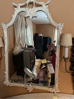 Full view of the ornate white hanging wall mirror reflecting room interior.