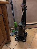 Full view of Shark Apex upright vacuum with attached hose and upright Swiffer mop with green handle standing beside it.