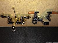 Photo showing two chrome bathroom faucets mounted side by side, one with wooden-style handles and one with round handles.