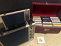 Photo showing the beige and blue 8-track tape player along with red case containing 15 8-track tapes.