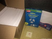 Box open showing approximately 500 white mailing envelopes stacked inside, partial view of two other paper packs to the right