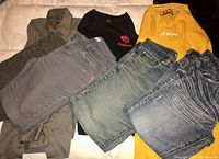 Photo displaying all clothing items laid out: yellow CCM hockey jersey, black Adidas Canada long sleeve shirt, grey-brown dress shirt, two older patched blue jeans, and two grey dress jeans.