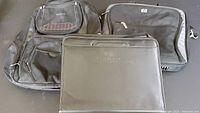 Photo showing Targus backpack with multiple zippers, HP laptop bag, and black leather Montgomery Ward portfolio folder placed side by side.