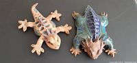 Top view photo showing both ceramic lizards side by side on a dark surface.