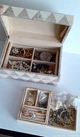 Top view of stone jewelry box lid open showing compartments with assorted jewelry inside and additional jewelry pieces outside the box on a white surface.