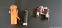 Photo showing vintage binoculars with brown leatherette and black eyecups next to a small black spy glass and tan leather case