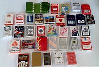 Photo showing 27 various playing card decks laid out in rows with different brands and designs visible.