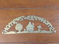 Close-up photo of a brass key holder featuring the words 'Home Sweet Home' with cat silhouette images and five hooks underneath, placed on a wooden surface.