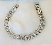 Photo shows a costume bracelet laid flat on a light surface. Bracelet consists of two rows of faceted clear white stones set in metal with a box clasp.