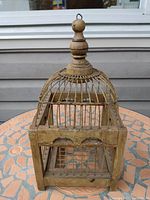 Front and side angle view of the decorative bird cage showing the dome shaped metal wire top with wooden finial and square wooden base frame.