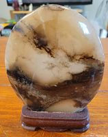 Front view of the oval polished stone with natural color variations mounted on a dark wooden base.