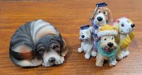 Photo of six dog resin figurines including one lying dog trinket box and five standing dogs with colorful hats.