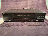 Front angled view of Emerson black VHS VCR with 4 head digital auto tracking label and control buttons.