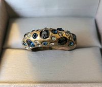 Front view of a gold-tone fashion ring embedded with multiple blue and clear round stones in a display box.