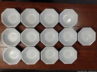 Thirteen white octagonal bowls arranged in a 3-3-4-3 formation showing the set quantity and shape.