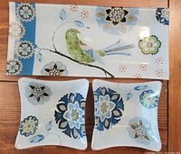 Photo of the three glass dishes showing one rectangular platter with bird and floral design, and two smaller square dishes with floral patterns.