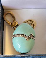 Close-up photo of Juicy Couture limited edition light blue egg-shaped charm with rhinestone detail and gold-tone clasp inside box.