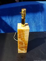 Rectangular marble lamp base with brass light socket and cord on black surface and blue background