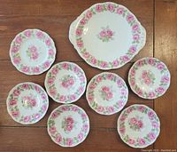Set of 6 saucers, 1 lunch plate and 1 cake platter with pink rose floral bone china pattern on wooden table.