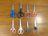 All eight scissors laid flat on wooden surface showing variety in size and handle colors.