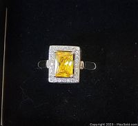 Top-down photo showing square cut yellow gemstone center surrounded by white stones in sterling silver ring.