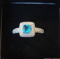 Front view of a sterling silver ring featuring a square blue center stone surrounded by white stones against a black background.