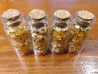 Four small glass vials filled with crumpled gold leaf sheets, standing upright with cork stoppers visible.