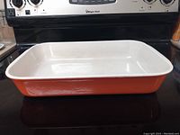 Side view of orange enameled cast iron lasagna pan on stove, showing exterior and interior edges