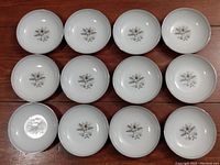 Twelve white ceramic bowls with floral Minuet pattern arranged on wooden surface