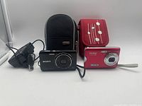 Photo showing Sony Cyber-shot camera, red Vivitar ViviCam camera, and two camera travel cases (black and red floral design)