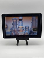 Front view of the Amazon Kindle tablet powered on showing lock screen with chess piece wallpaper and lock icon.