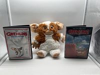 Front view of Gizmo plush figure flanked by Gremlins Special Edition DVD on the left and Gremlins 2 DVD on the right.