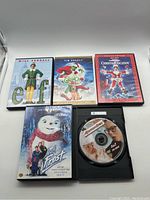 Front view of 4 DVD cases Elf, The Grinch, Christmas Vacation, and Jack Frost with an open DVD case showing disc of A Christmas Story