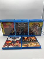 Front view of six Blu-Ray movie cases arranged with three standing in back and three laid flat in front, showing cover art and titles clearly.