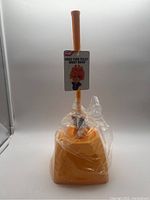 Full view of the orange toilet brush with stand, sealed in plastic wrapping. Tag attached reads 'MAKE YOUR TOILET GREAT AGAIN'.