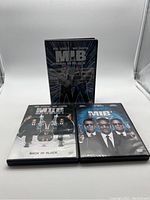Front view of three Men In Black DVD cases including the original standing case, and two standard DVD cases for MIB 2 and MIB 3.