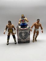 Three WWE wrestling figures displayed standing and seated on a WWE box.