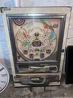 Full front view of the Nishijin Super Deluxe panchinko machine showing the glass playfield with metal balls and colorful targets, exterior wood grain finish, control lever, and lower panel.