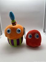 Photo of two plush toys: an orange Five Nights at Freddy's cupcake plush and a red Pac-Man ghost plush.