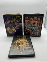 Front view of three WWE wrestling DVDs displayed upright: Jeff Hardy My Life My Rules with purple and yellow cover, WrestleMania 22 featuring multiple wrestlers on front, Ric Flair & The Four Horsemen with gold-tinted image on front.