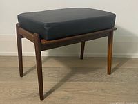 Front-left angle view of teak footstool with black cushion