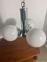 Front angle view of the chrome spindle style chandelier with three white glass globes showing reflectivity and condition.