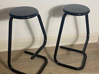 Front perspective of pair of stools showing paperclip-shaped tubular metal frames and round seats
