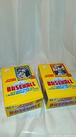 Two bright yellow full unopened boxes of 1990 Score Major League Baseball cards with packs, showing front side of boxes with player photos and text.