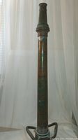 Full front view of tall antique fireman's water hose nozzle showing pipe-like copper structure, patina, and extended length.